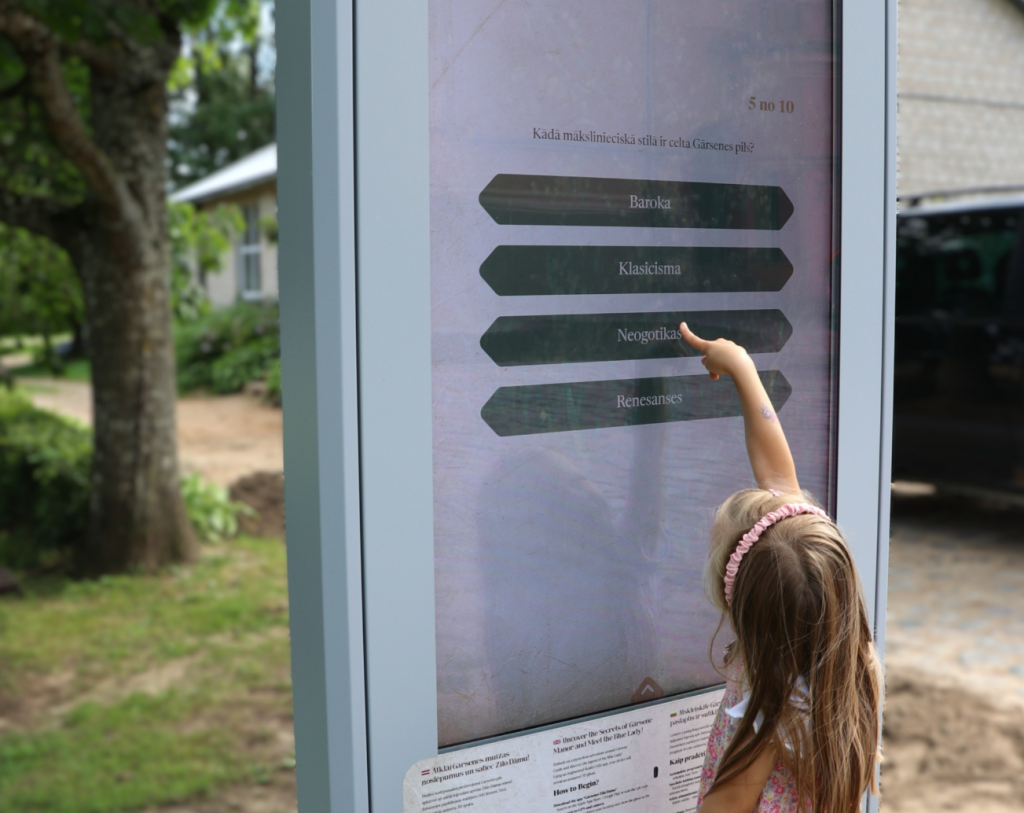 Gārsenes gids viedtālruņa ekrānā muižas parkā